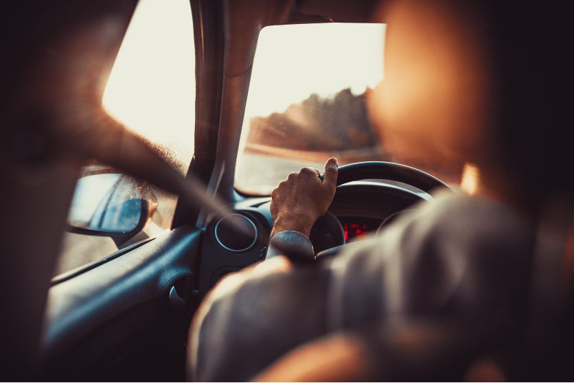 the image shows a close up of a driver with hands on the wheel and a road with a sunset in the distance, representing an article about motor vehicle accidents.