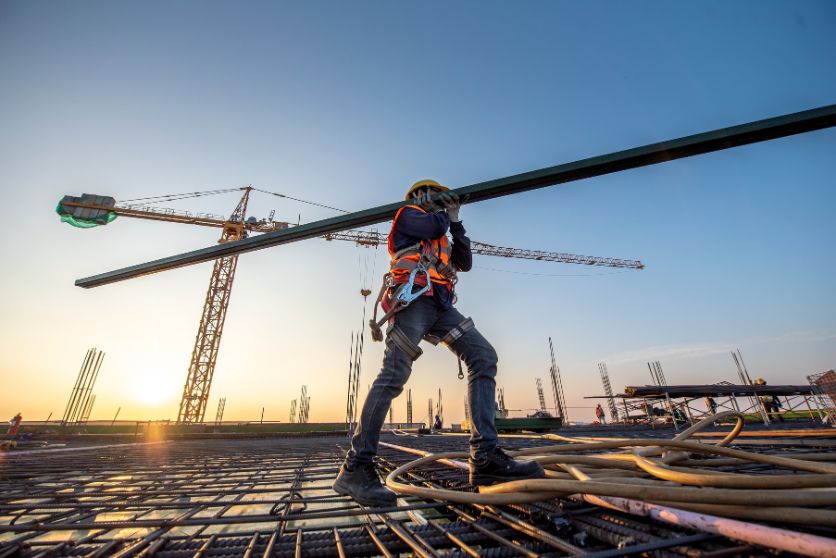 the image shows a construction site with a man carrying a beam, representing an article discussing 4 commonly overlooked dangers in the workplace.
