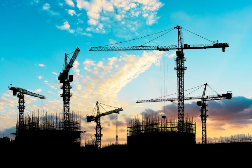 the image shows construction cranes against a blue sky, representing an article on crane accident lawyers. 